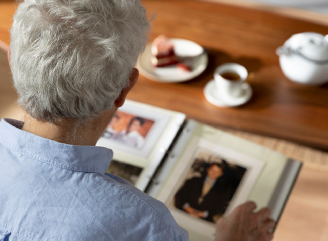 Elderly person viewing family photo album at a table with tea